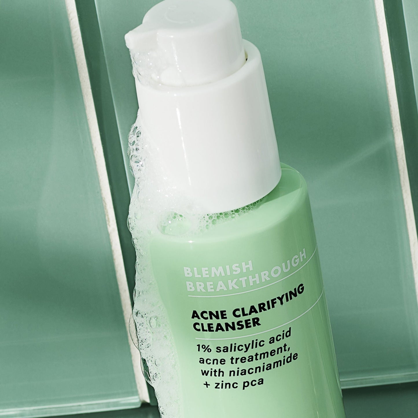 Green bottle of Acne Clarifying Cleanser with white pump on a green background